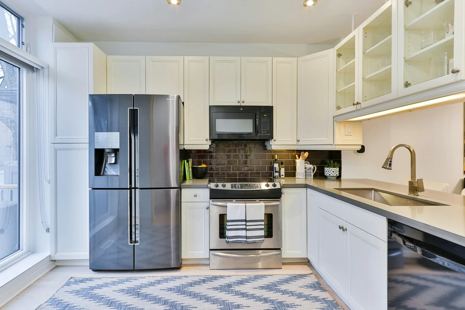 Modern kitchen in a Regina home with a stainless steel refrigerator, range, and over-the-range microwave.